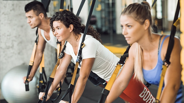 Drei Sportler trainieren gemeinsam an TRX Bändern in Augsburg und konzentrieren sich auf ihre Körperhaltung.