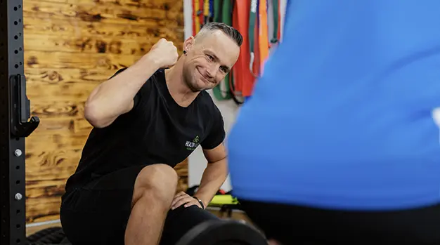 Marco Neumann feuert einen Kunden mit einer geballten Faust an, während er sich in einem Fitnessstudio in Neusäß für das Training vorbereitet.