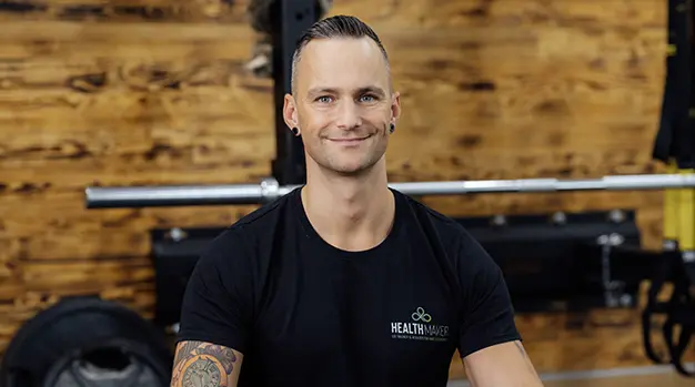 Marco Neumann, Personal Trainer in Gersthofen, steht in schwarzer Trainingskleidung mit verschränkten Armen und lächelt in die Kamera.