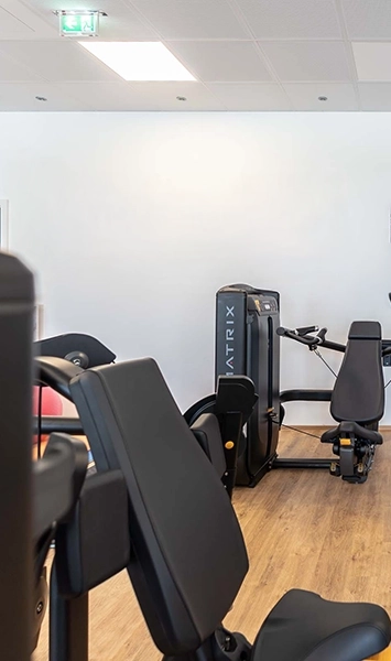 Das Bild zeigt einen hellen Fitnessraum mit modernen Kraftgeräten der Marke Matrix. Holzoptik-Boden und klare Raumgestaltung sorgen für eine freundliche Atmosphäre.