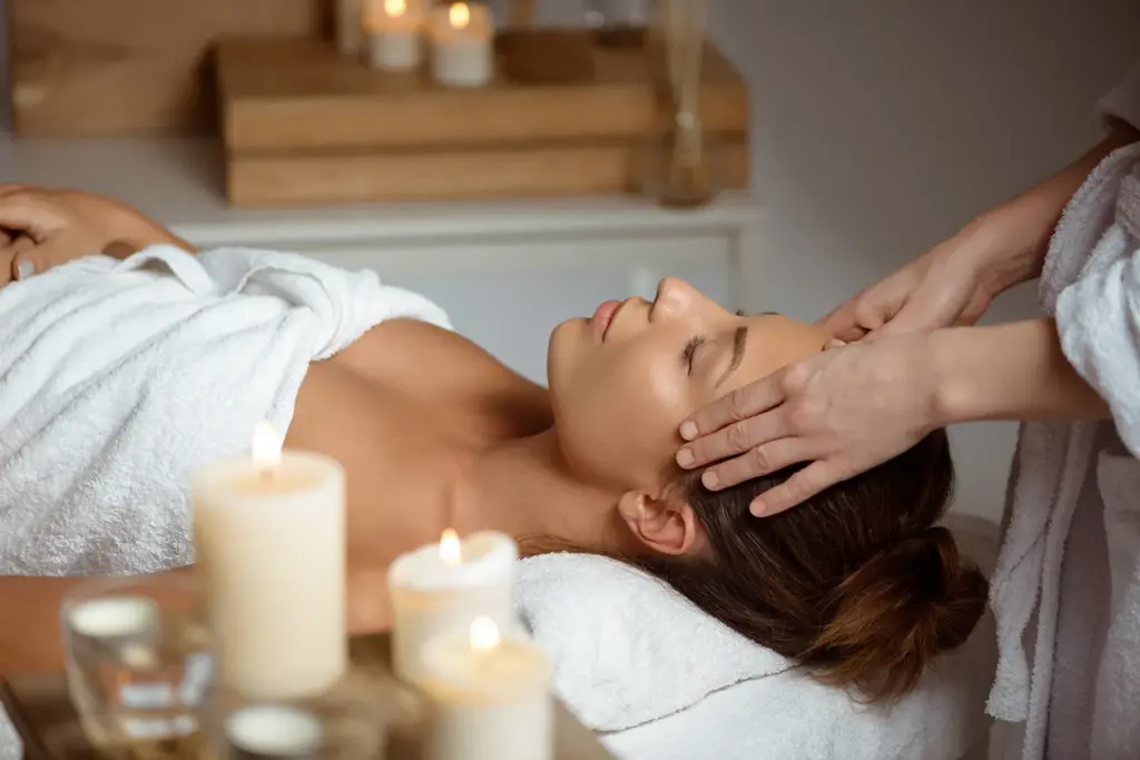 Alpha Reset Massage in Augsburg bei der eine junge Frau eine entspannende Gesichtsmassage in einem Spa mit Kerzenlicht im Hintergrund erhält