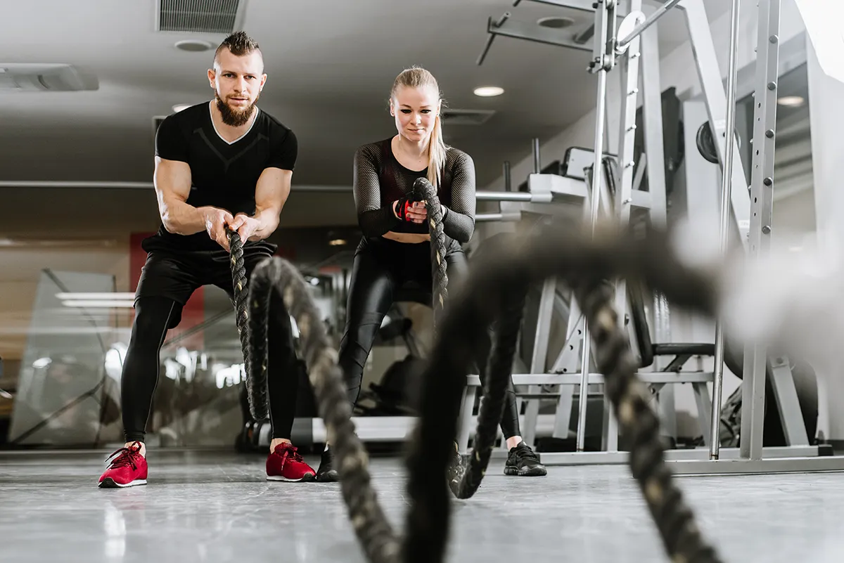 Zwei sportliche Menschen beim funktionellen Krafttraining mit Battle Ropes im Fitnessstudio. Effektives Training zur Fettverbrennung und zum gezielten Bauchfett loswerden.