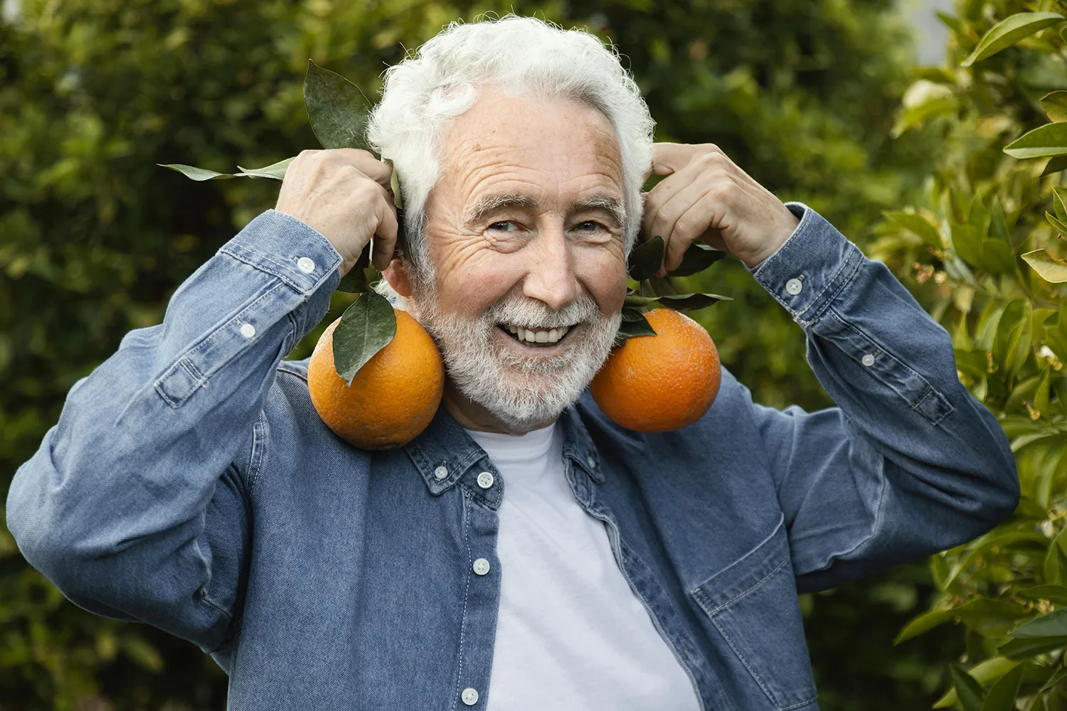 Ein älterer Mann zeigt mit einem Lächeln zwei Orangen als Sinnbild für gesund altern durch vitaminreiche Ernährung und Lebensfreude