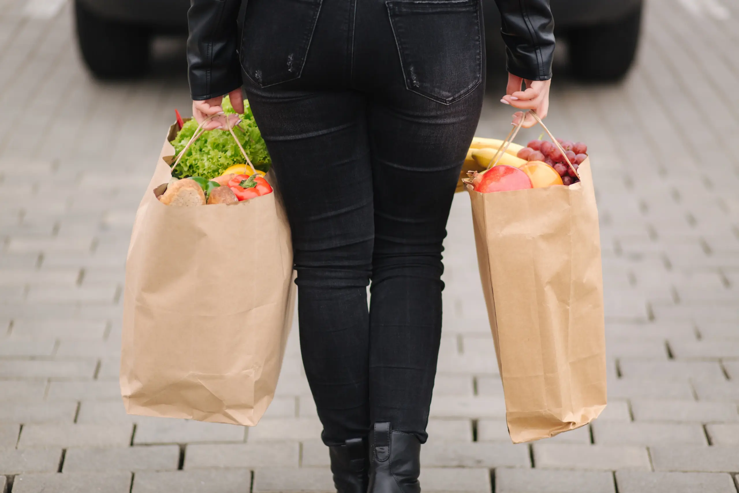 Frau trägt eine Einkaufstasche mit frischem Obst und Gemüse, Symbolbild für gesunde Ernährung